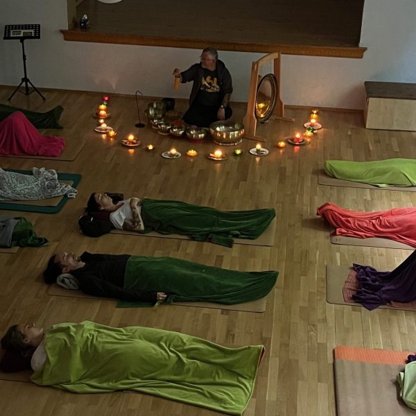 Ricardo umgeben von Klangschalen, im Hintergrund; im Vordergrund liegen Teilnehmer entspannt auf Yogamatten