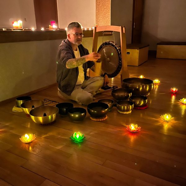 Riccardo schlägt einen Gong während eines Klangbads bei Yoga in Neuzelle, umgeben von bunt leuchtenden Teelichtern