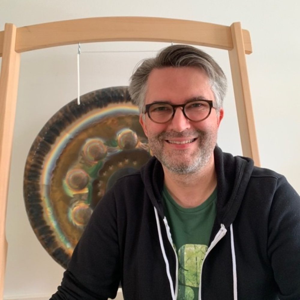 Ricardo Liebsch, Leiter des Klangbads, mit Gong im Hintergrund in entspannter Haltung